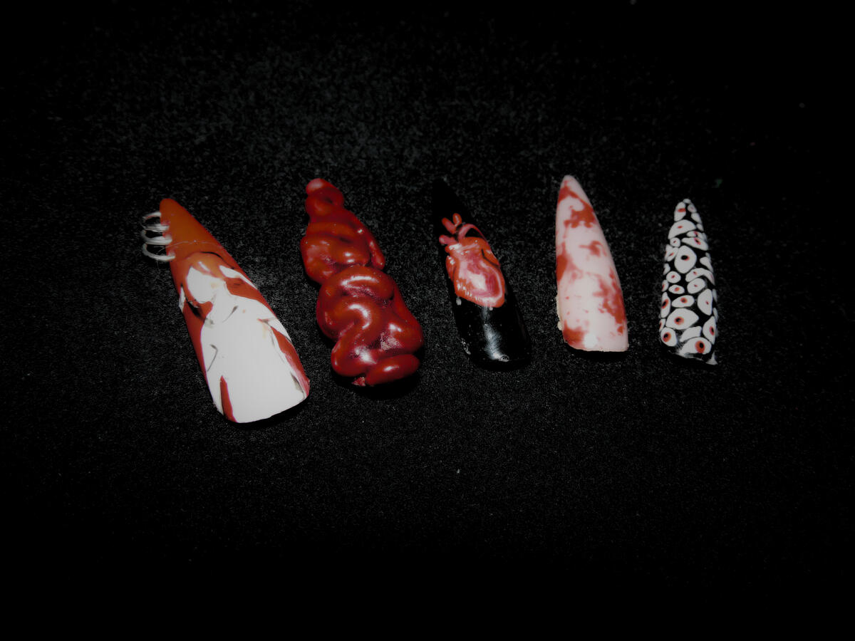 Untitled Gothic horror-inspired press-on nails displayed on a black background. The set has long pointed nails with red, black, and white designs including blood splatter effects, realistic anatomical heart art, silver ring piercings, and a multitude of eyes.